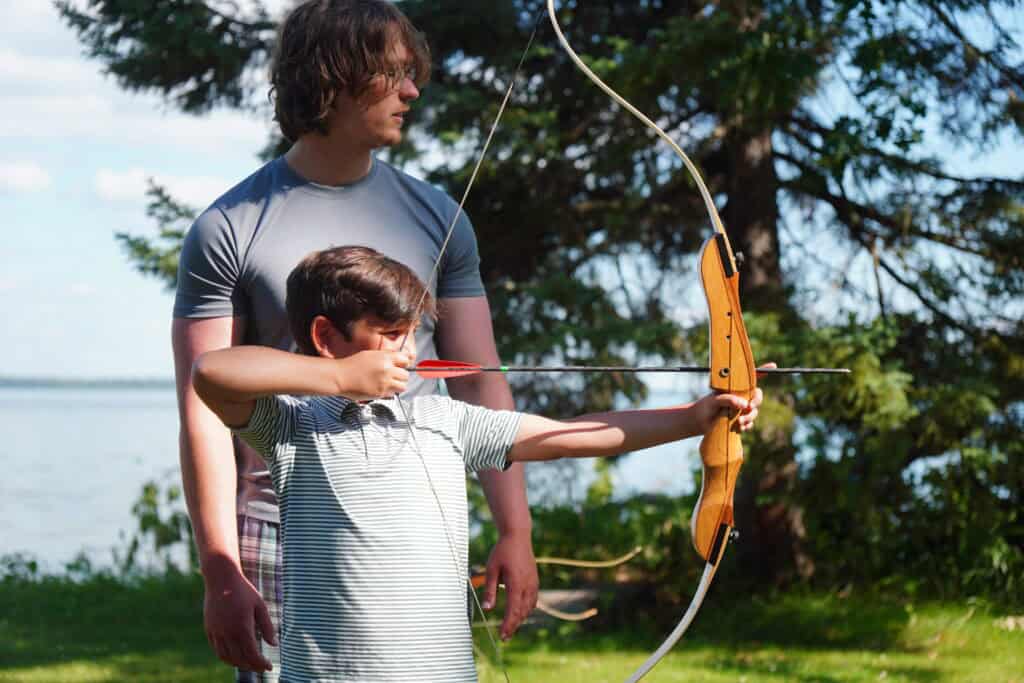 a counselor teaches a camper learns to shoot archery