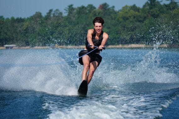 camper smiling while waterskiing on beautiful lake during summer camp.