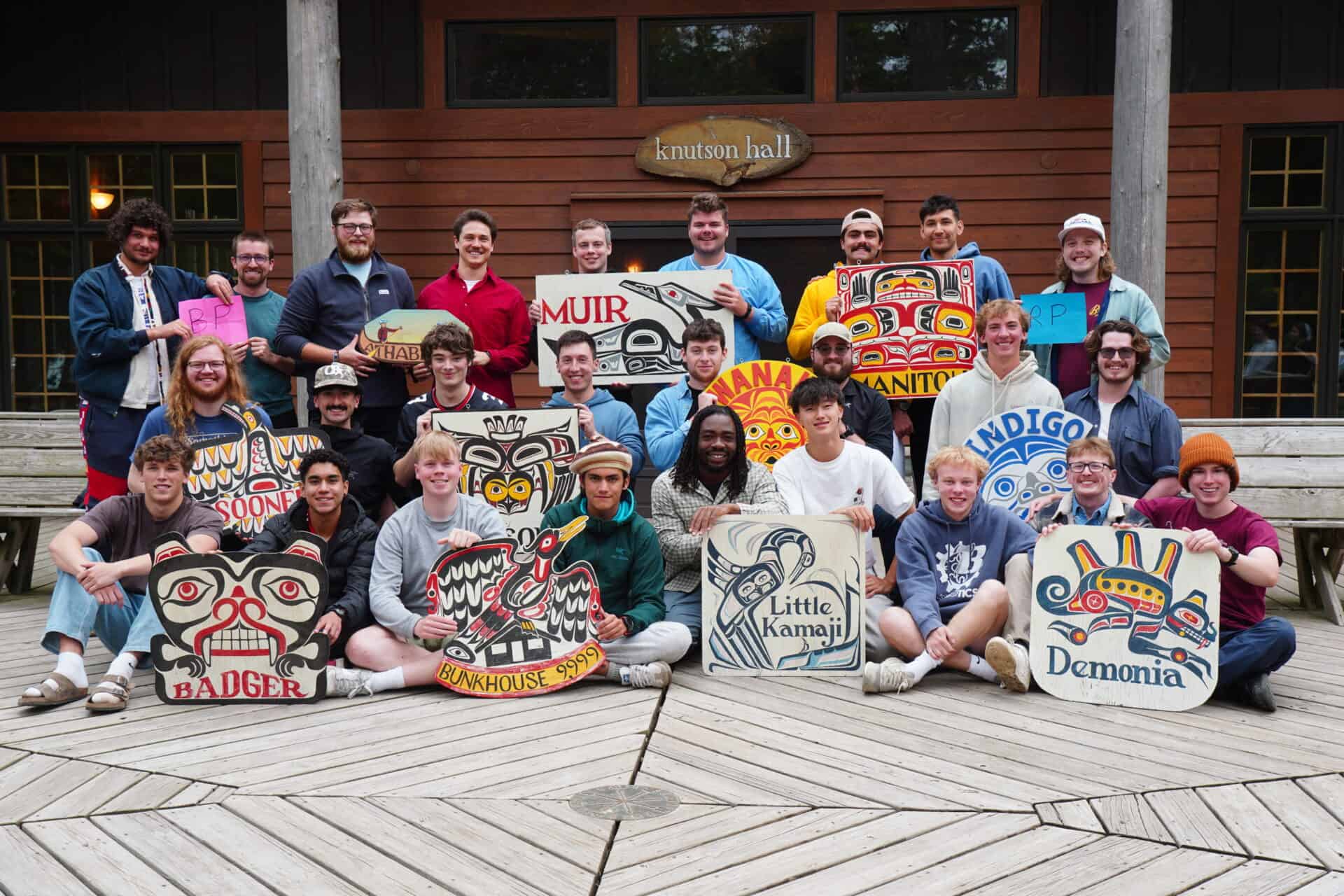 staff smiling and holding cabin signs at summer camp.