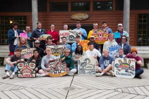 staff smiling and holding cabin signs at summer camp.