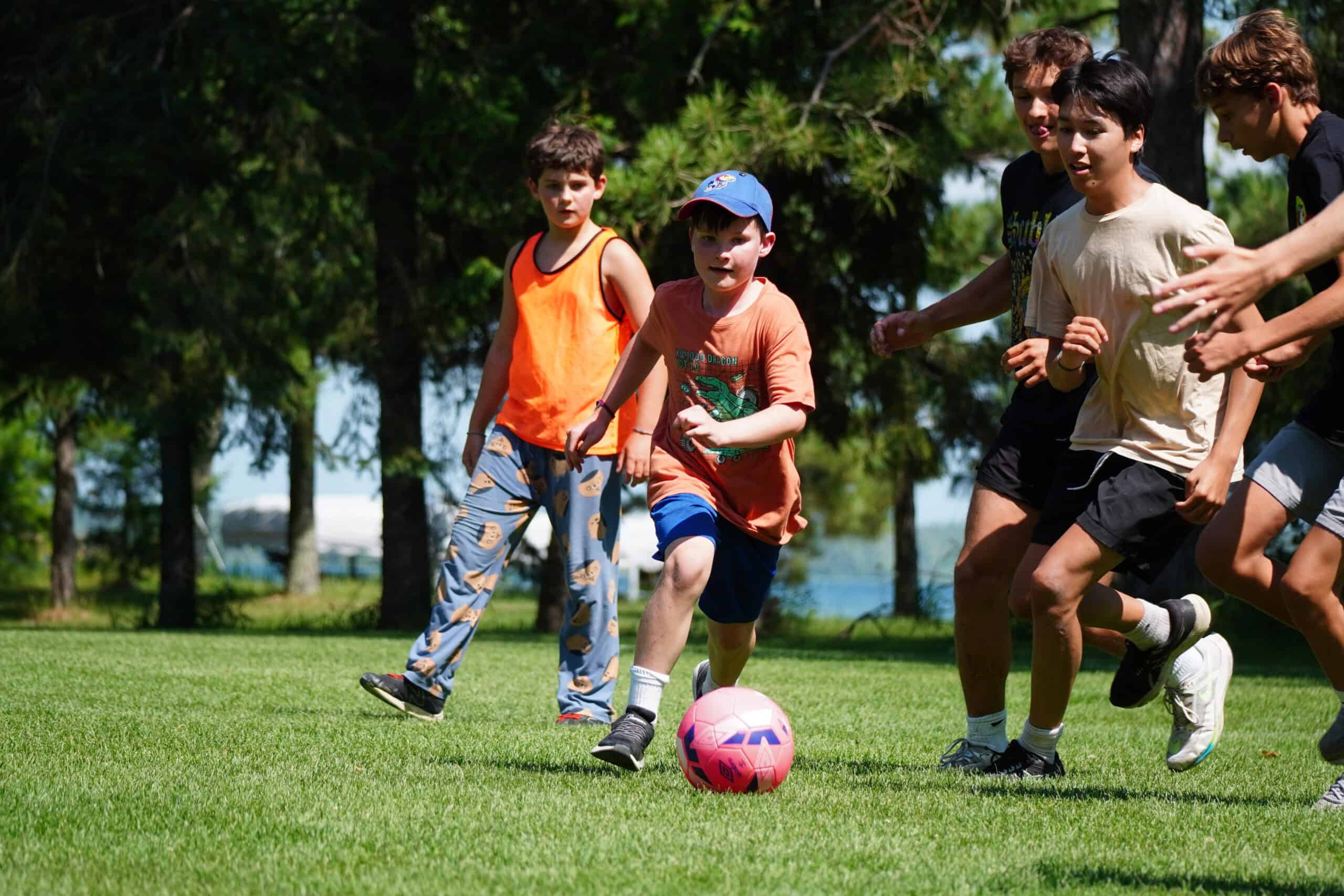 boys chasing soccer ball on field with lake in background.