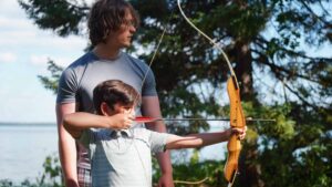counselor teaching camper to shoot archery.