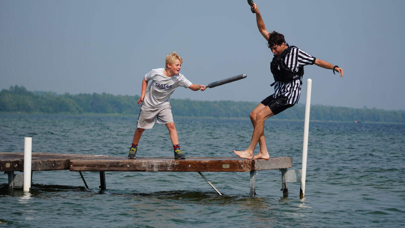 boy with fake sword knocking another boy into lake.