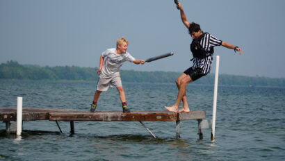 boy with fake sword knocking another boy into lake.