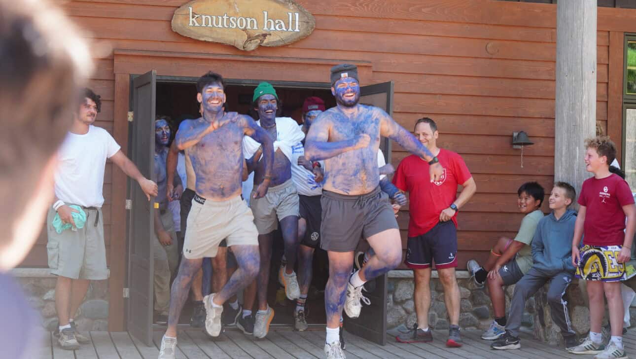 two men painted in blue dancing on deck.